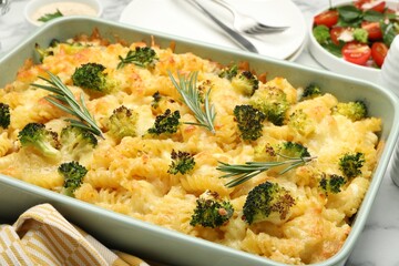 Tasty pasta casserole with cheese, rosemary and broccoli in baking dish on table, closeup