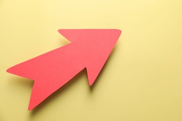One red paper arrow on yellow background, top view. Space for text