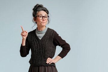 A 50-year-old woman, a school teacher with a stern look, her hair tied in a bun. She has one hand on her hip and the other with a finger pointing up, indicating something.