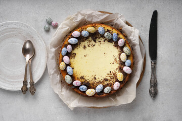 Homemade Easter cheesecake, sweet cottage cheese baking, with Ester chocolate eggs on light table with plate nearby, top view