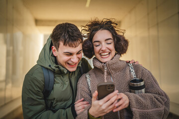 young couple boyfriend and girlfriend stand outdoor and use cellphone