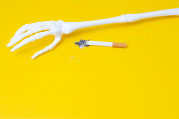 Hand of skeleton with burned cigarette and ash as a symbol of danger which is in smoking separated...