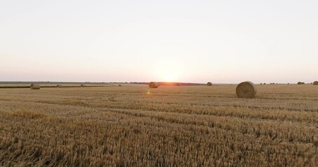 Aerial perspective of straw bales arranged across dry fields, set breathtaking sunset aerial view. Rch textures of cut hay and rolling land form a serene countryside composition. - Powered by Adobe