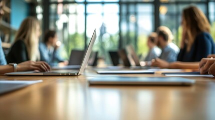 Professionals engaged in a collaborative meeting around a large table, using laptops and documents. Bright, modern office environment with natural light and focus on teamwork