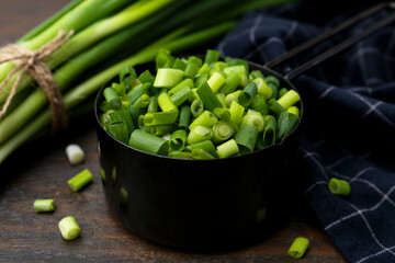 Chopped green onion in saucepan and stems on wooden table, closeup