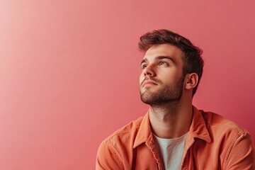 Obraz premium Thoughtful Young Man in Casual Attire Against a Soft Pink Background