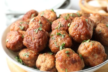 Tasty cooked meatballs with green onion in bowl on white table, closeup