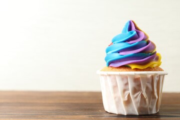 Delicious cupcake with colorful cream on wooden table against white background, closeup. Space for...