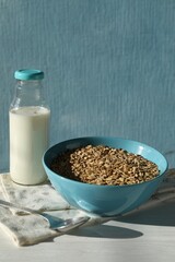 Tasty oatmeal in bowl and milk served on white wooden table against light blue background, space for text