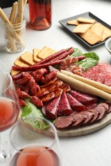Different smoked sausages and other snacks served with wine on white table, closeup