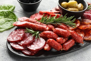 Different smoked sausages, olives and rosemary on grey table, closeup