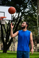 A young man is shown enjoying playing basketball outdoors, with a bright smile and surrounded by trees, showcasing a love for outdoor sports and recreational activity.