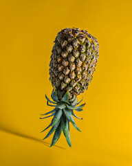 Upside-down pineapple standing on yellow surface against matching background. Surreal fruit...