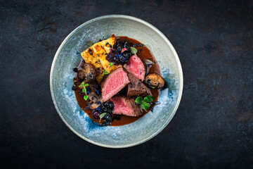 Barbecue dry aged venison steaks - deer entrecote cut English roasted with grilled mushrooms, fruit berry gravy sauce and panettone herbs served as top view on a design plate with copy