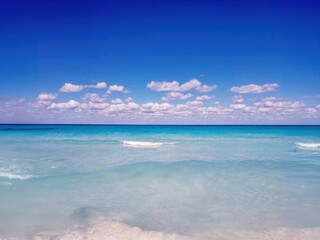 Obraz premium Crystal Clear Turquoise Ocean With Gentle Waves and White Clouds in a Vibrant Blue Sky at a Tranquil Beach