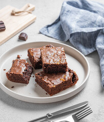 Chocolate brownie with nuts cut into pieces on a plate on a light background with fork and napkin.