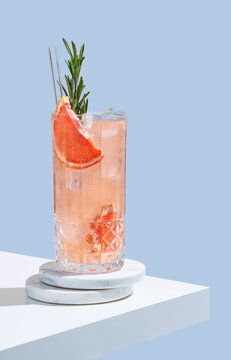 Refreshing mocktail with grapefruit, rosemary and ice in a glass on a blue background with shadow.