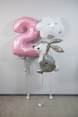 composition of balloons for a girl: pink number two, gray bunny and white cloud, helium balloons bunch with confetti