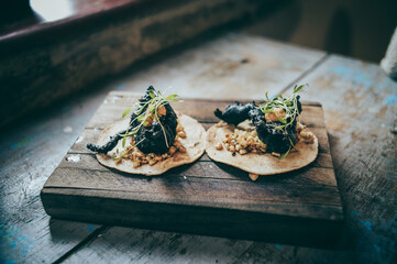 Charcoal crab tacos with corn kernels, served on a wooden board.