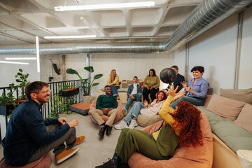Coworkers playing with a bowling ball in modern office relaxing on beanbags