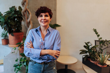 Fototapeta premium Confident businesswoman smiling with crossed arms in modern office with plants