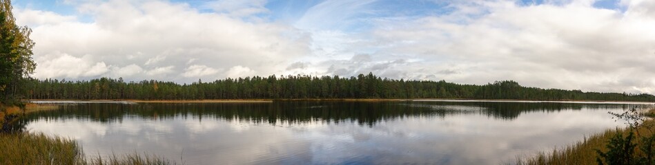 Tranquil Lake Reflecting Expansive Sky and Dense Evergreen Forest in Remote Wilderness During Autumn Season