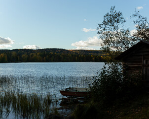 Rustic Wooden Boathouse Overlooking Calm Lake with Small Rowboat Amidst Autumn Landscape in Finnish Countryside