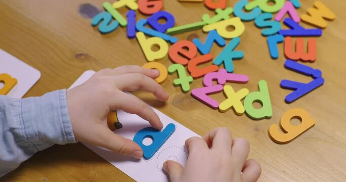 Close-up of girl's hands making an English word on a game card on a wooden table. Learning to read in English. Home-schooling. Education. Literacy.