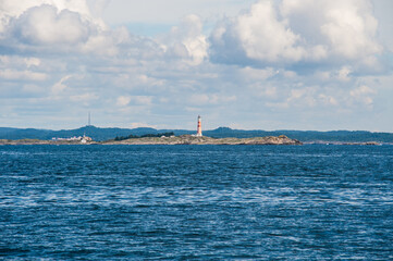 Kristiansand, Norway - August 04 2010: distant lighthouse on rocky island in sea.