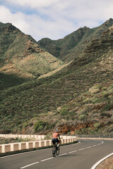 Cyclist riding a road bike on a scenic mountain road.  Stunning landscape with vibrant green hills and clear blue sky. Perfect for travel, adventure, and active lifestyle themes.