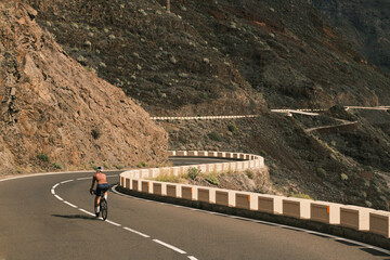 Fototapeta premium Cyclist rides along a scenic mountain road with sharp curves and stunning views. Perfect for travel, adventure, and active lifestyle themes.