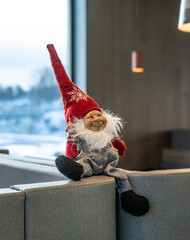 gnome figurine with red hat and white snowflake pattern sitting on couch with snowy window...