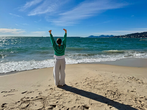 A woman standing on a serene beach, arms lifted for stress relief and mental clarity. Coastal calm, personal rejuvenation, digital detox
