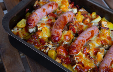 Baked vegetables with homemade sausages served in baking tray on wooden table
