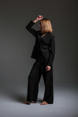 Stylish model poses confidently in a black suit against a dark backdrop during a studio photoshoot...