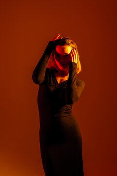 Woman in black dress poses under warm orange light in a creative studio setting