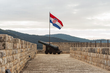 Historical cannon in the town of Ston, Croatia. A flag flies above the cannon-2.
