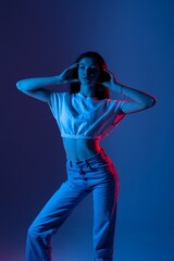 Obraz premium Young woman poses dramatically in stylish outfit with colorful lighting during studio shoot