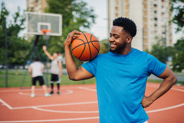 Naklejka premium Smiling basketball player holding ball on shoulder on court