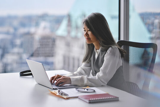 Busy middle aged Asian business woman using laptop working in office. Mature chinese professional businesswoman ceo at work, smiling female company executive manager looking typing at computer.