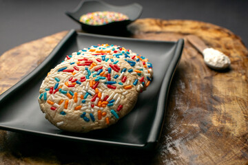 Colorful cookies sprinkled on black plate on a wooden table