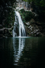 Obraz premium A serene waterfall cascading into a calm pool surrounded by lush vegetation and rocky cliffs, creating a peaceful and scenic natural retreat