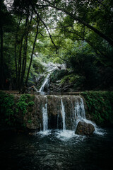 A picturesque multi-level waterfall in a dense forest, surrounded by vibrant green foliage. The cascading water creates a serene ambiance, perfect for nature lovers and eco-tourism