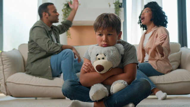 Sad little child boy hug teddy toy while mom dad fighting screaming arguing upset kid son suffer feel lonely parents conflict divorce fight psychological trauma problem custody in multiracial family - Powered by Adobe
