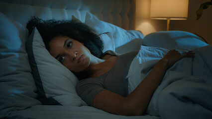 Noisy neighbours problem annoyed African American frustrated displeased woman lying in bed night...