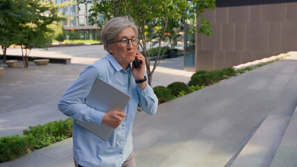 Caucasian mature 50s old woman businesswoman business employer walking up stairs going upward office building in city talking phone check time looking at wrist watch late rush hurry running lateness