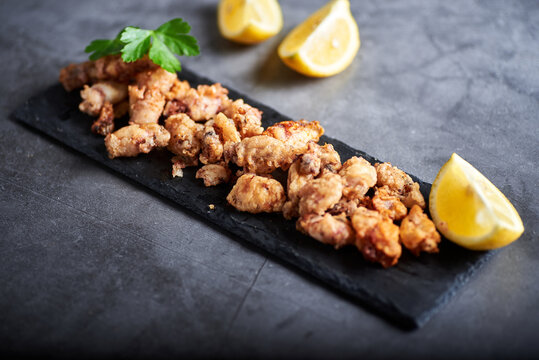 chipirones sobre un fondo de concreto en un plato negro con imagenes cenitales y acompa&ntilde;ado de limones todo con colores neutros.