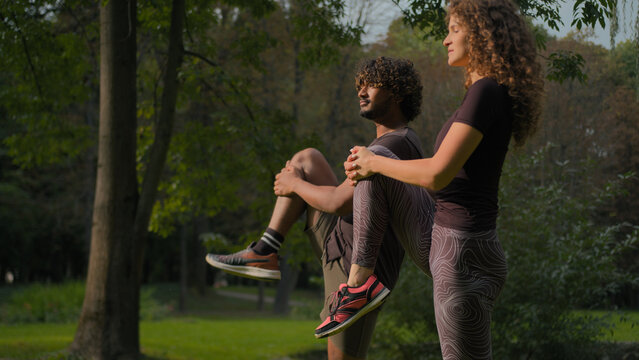 Multiracial fitness couple man woman stretching together outdoors workout yoga exercise morning sport practice with personal trainer athletic diverse sportswoman and sportsman training in nature park