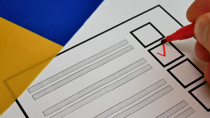 Voting in Ukraine. Voters hand using red marker to select candidate. Checkmark placed in checkbox. Background with Ukrainian flag. Representation of electoral participation, political choice