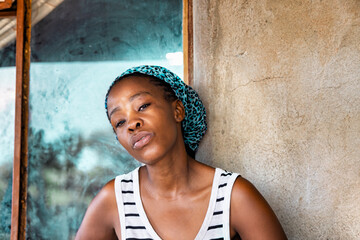 African village, portrait single African young woman standing in the yard , in front of the house,...